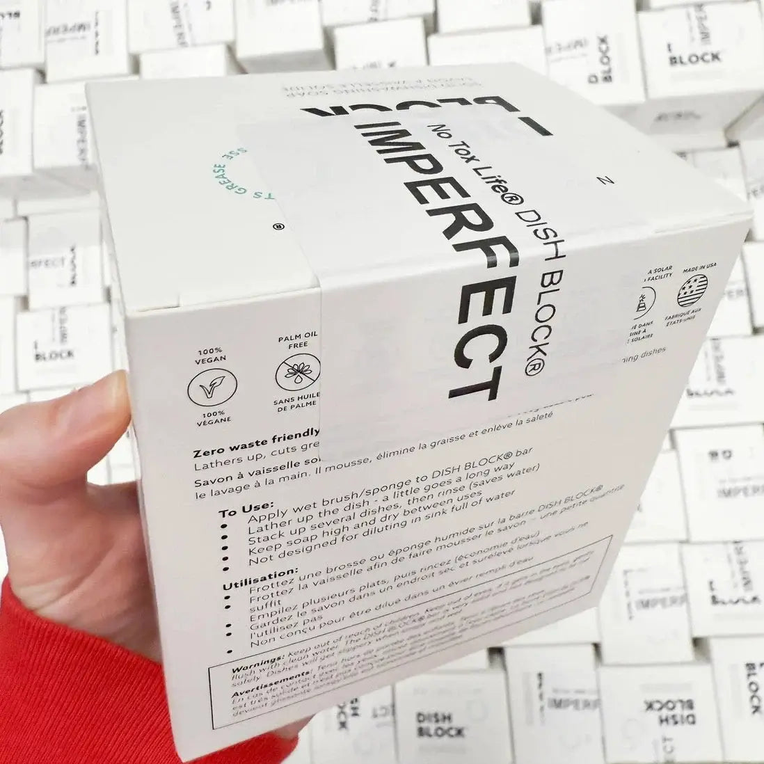 Hand holding a box of Dish Block Imperfect with white background