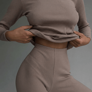 Person wearing a beige ribbed sweater and pants against a gray background