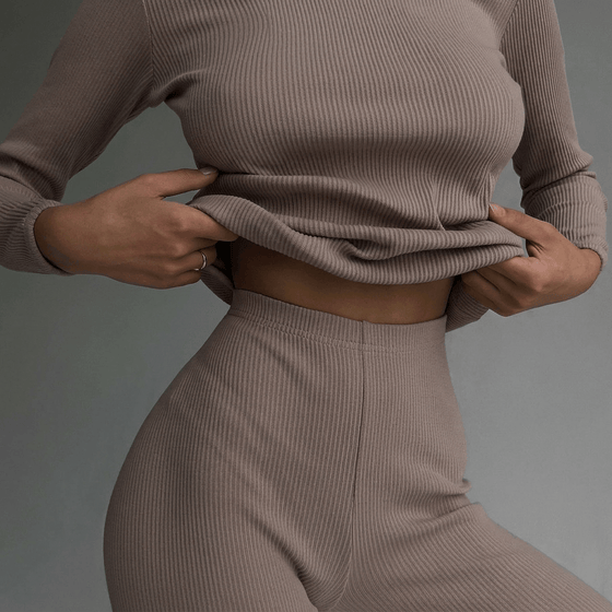 Person wearing a beige ribbed sweater and pants against a gray background