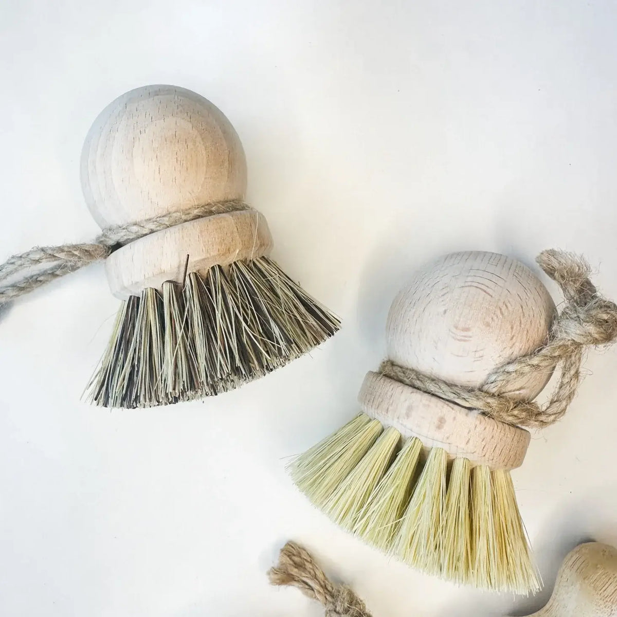 Two wooden ball tassels with natural fibers on a white background