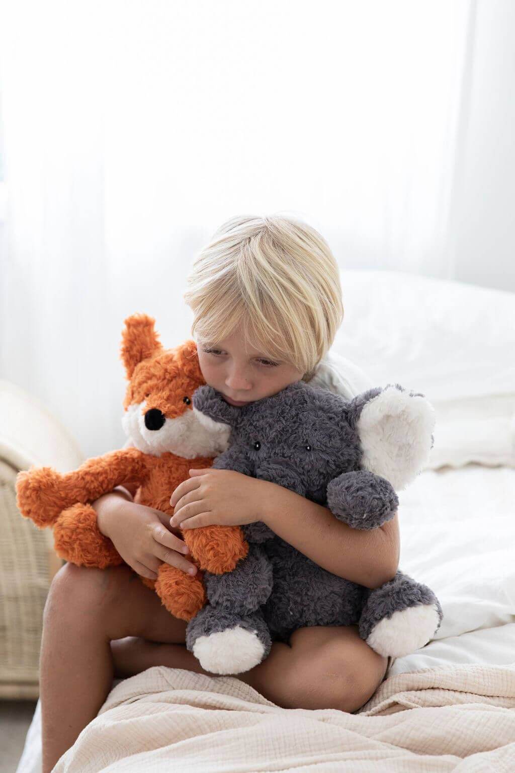A child cuddling Eleanor The Weighted Elephant and a fox plush toy for comfort.