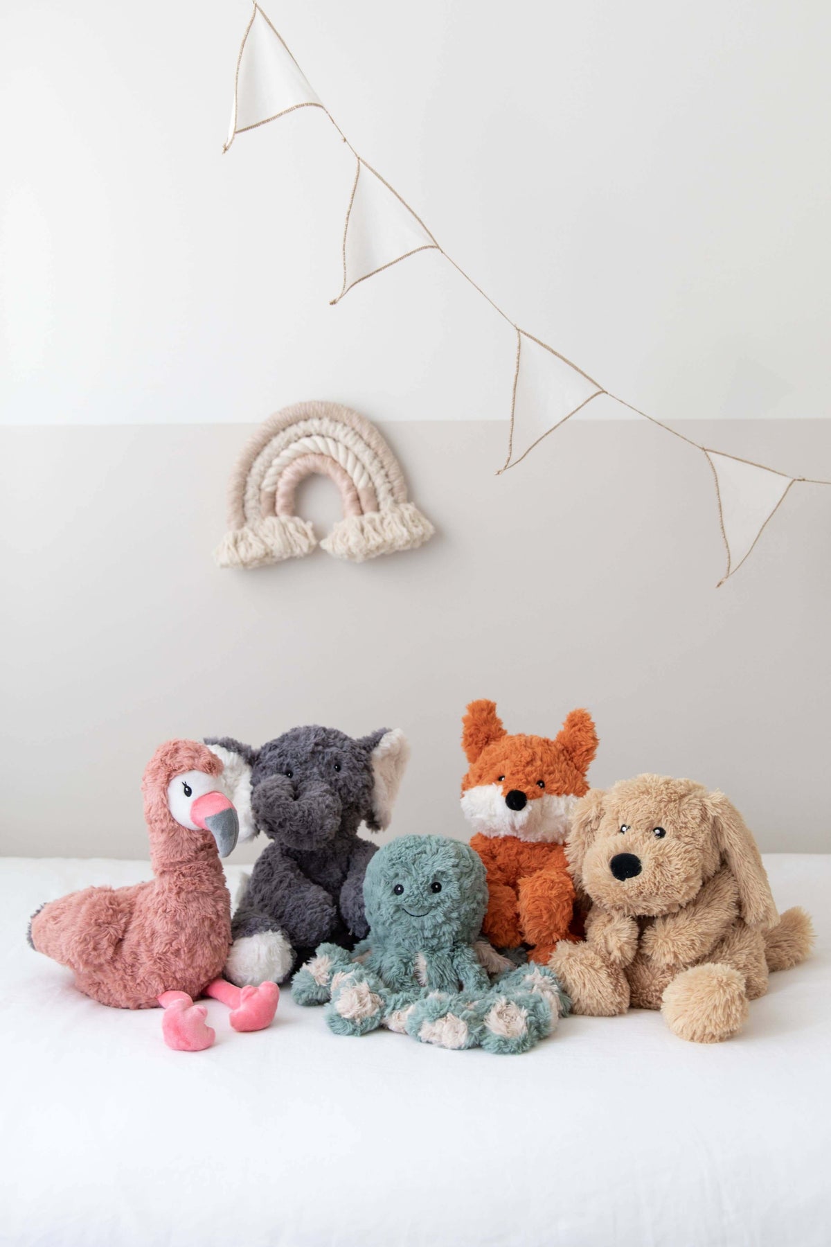 Eleanor The Weighted Elephant plush toy among colorful cuddly friends on a soft bed.