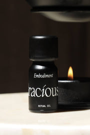 Embodiment Essential Oil Blend in a small black bottle next to a candle, promoting grounding and self-connection.