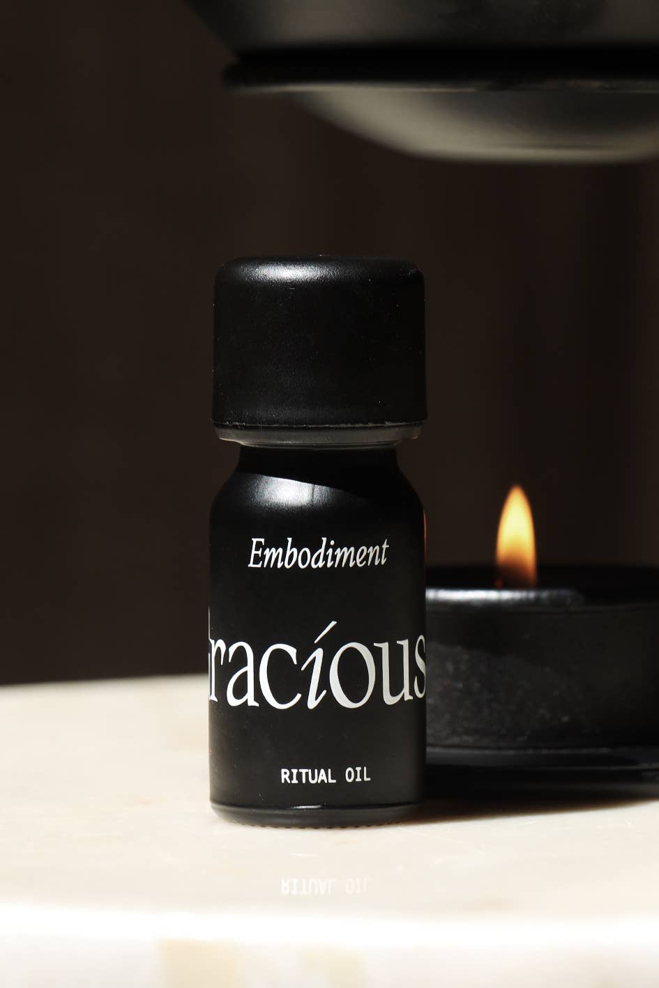 Embodiment Essential Oil Blend in a small black bottle next to a candle, promoting grounding and self-connection.