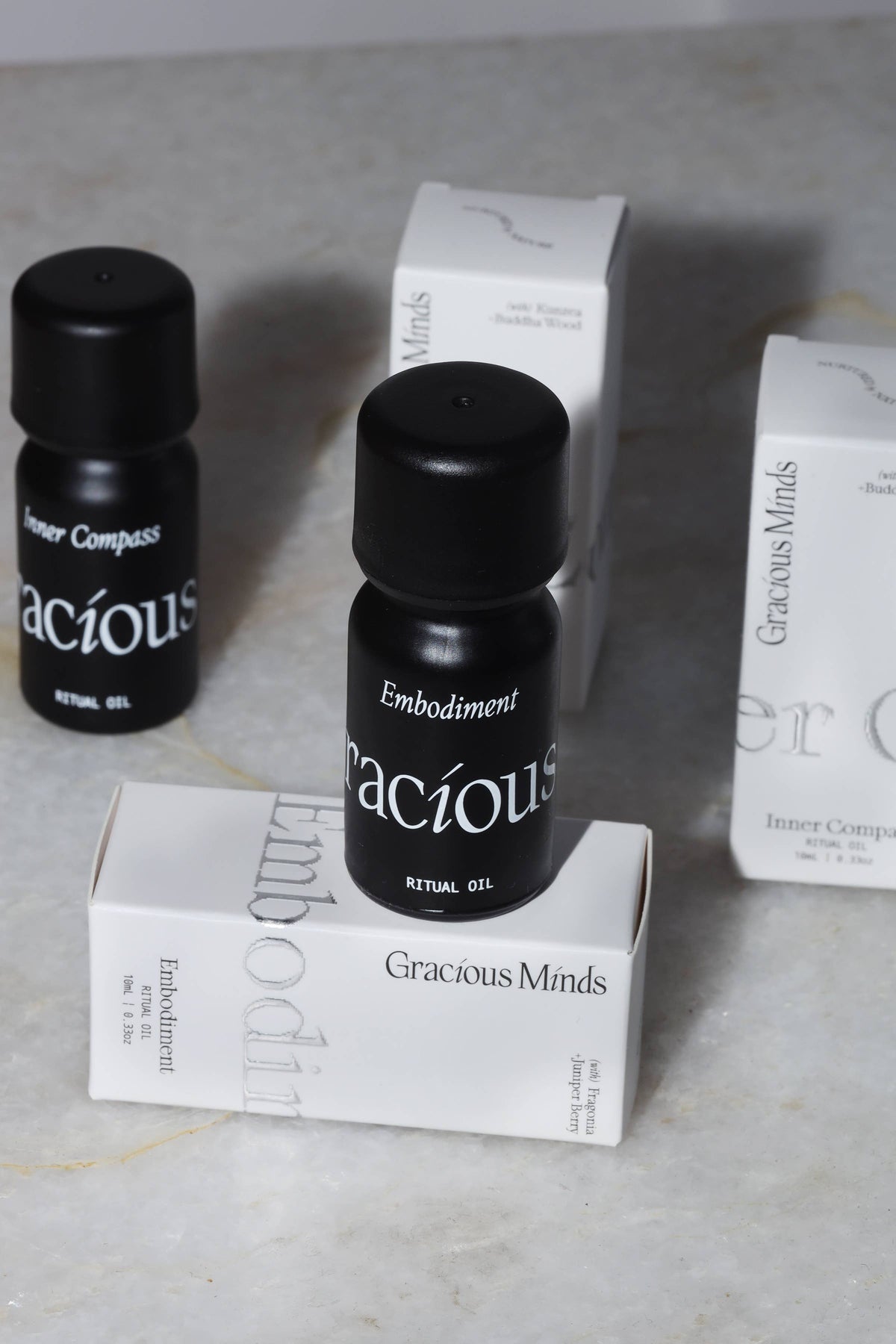 Embodiment Essential Oil Blend in sleek black bottle, surrounded by Gracious Minds packaging on a marble surface.