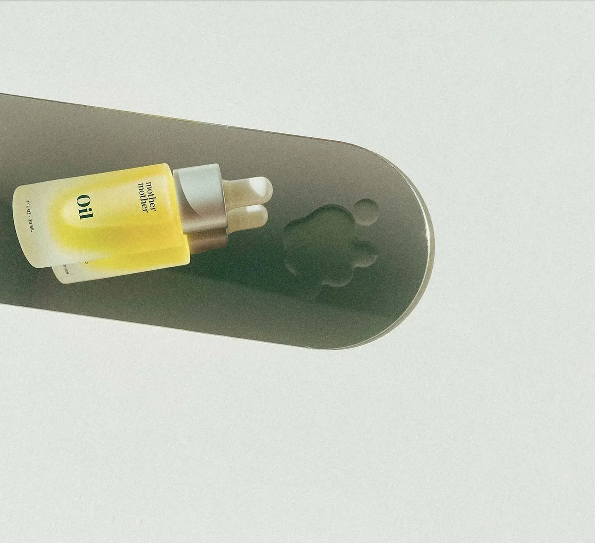 Two bottles of 'Oil' product on a gray surface with a white background