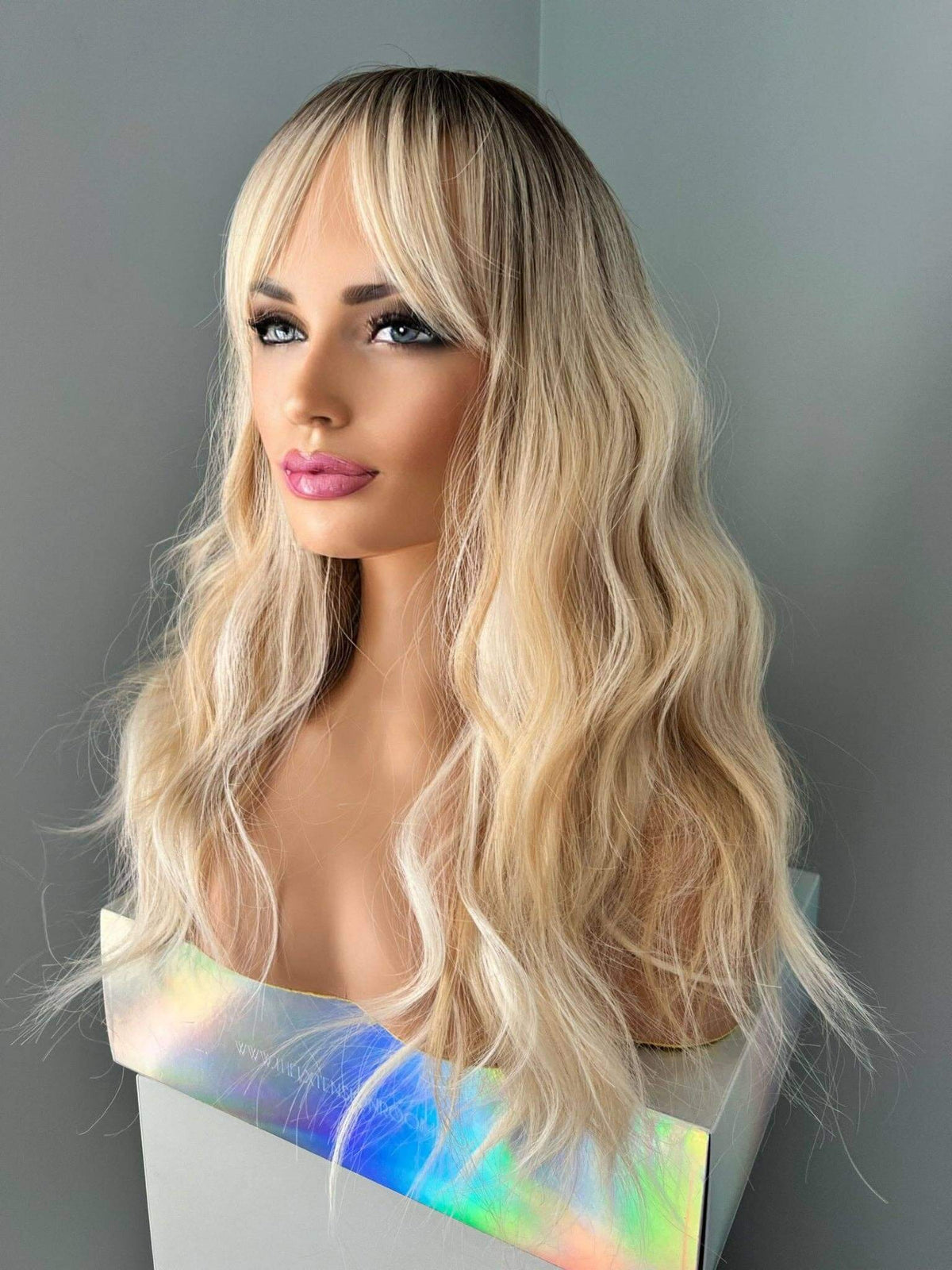 Blonde wig with wavy hair styled on a mannequin head against a gray background