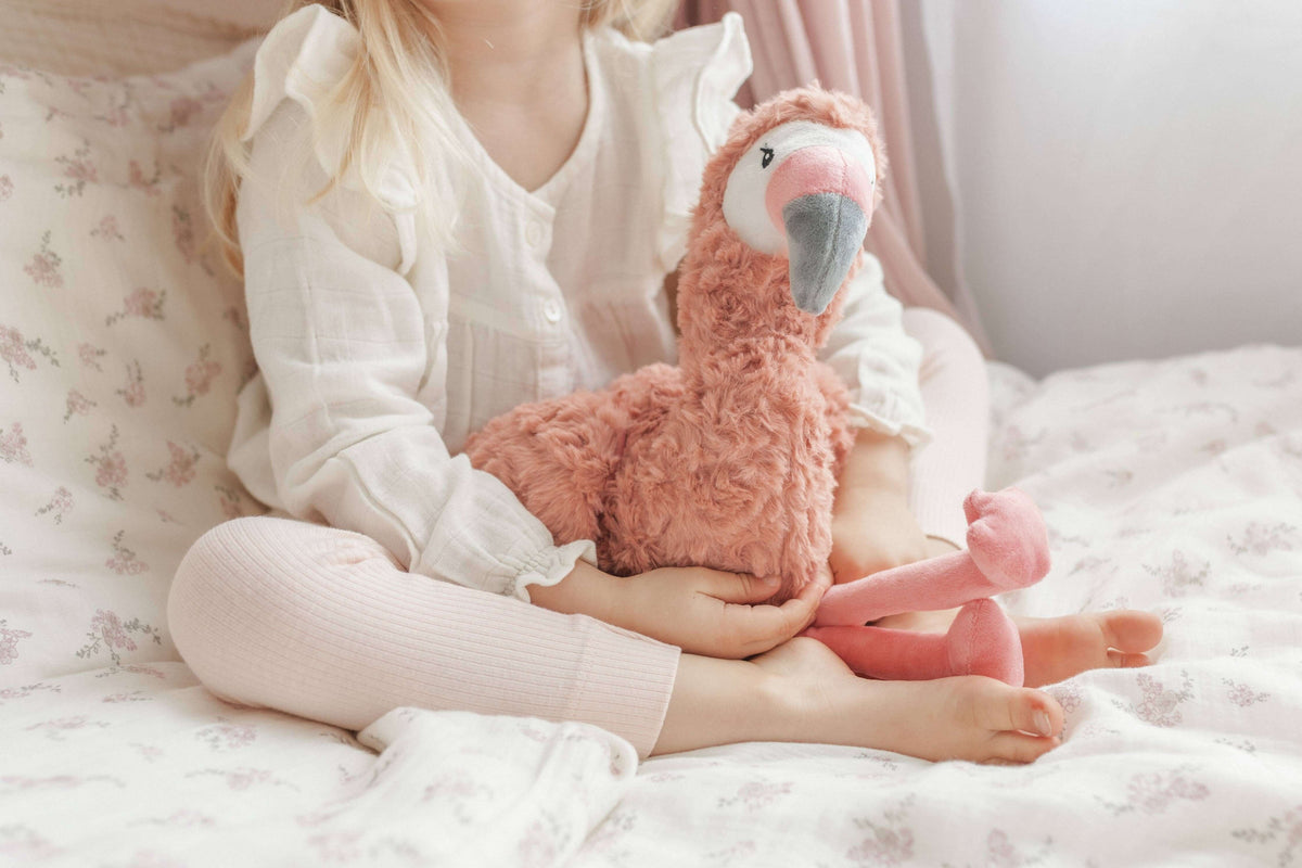 Child holding Francesca The Flamingo Weighted Teddy on a cozy bed, providing comfort and emotional support.