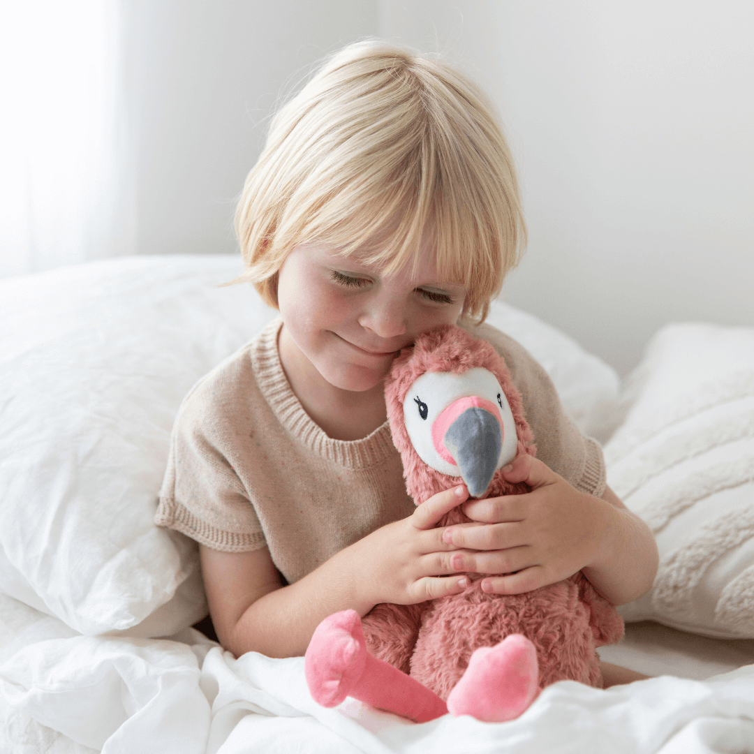 Child hugging Francesca The Flamingo Weighted Teddy plush toy in a cozy bedroom setting.