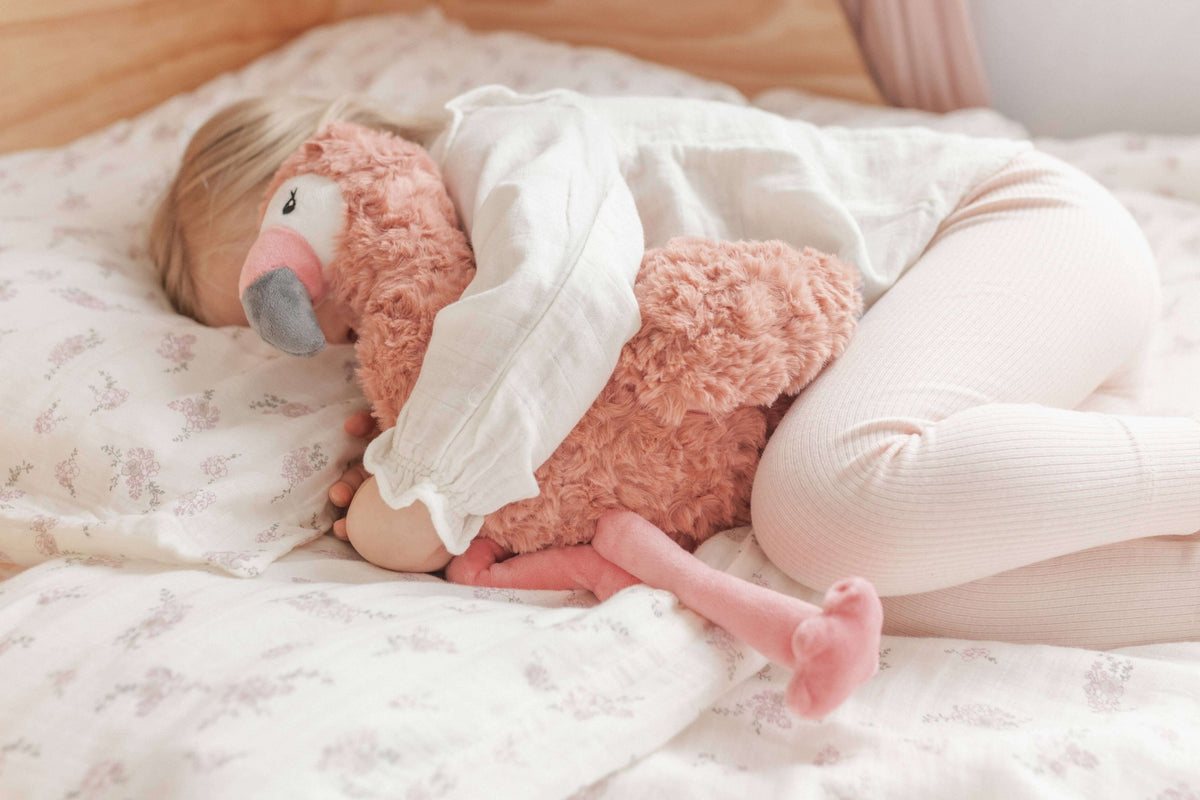 A child cuddling Francesca The Flamingo Weighted Teddy on a cozy bed, offering comfort and emotional support.