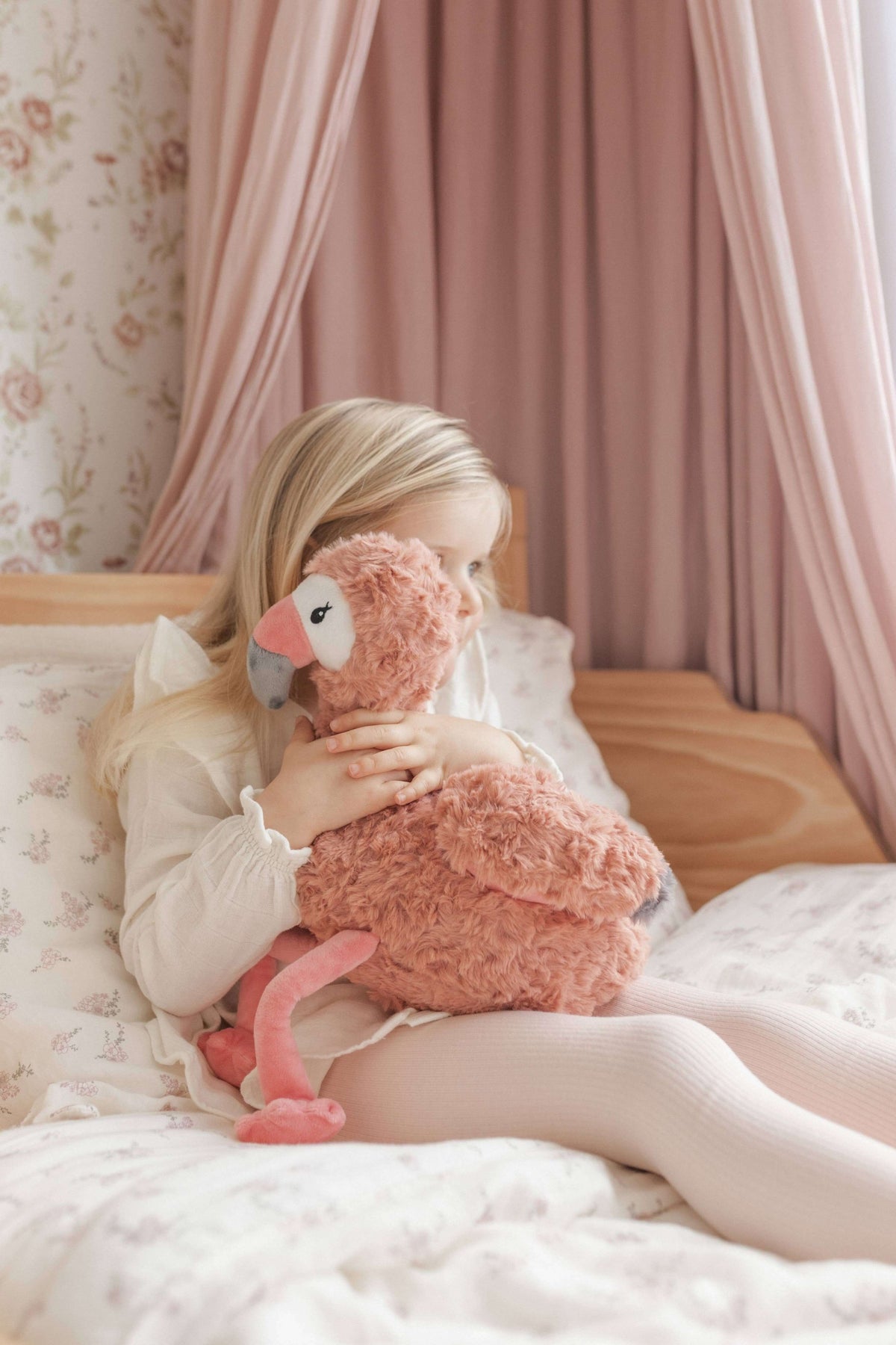 A child hugging Francesca The Flamingo Weighted Teddy on a cozy bed, promoting comfort and emotional support.