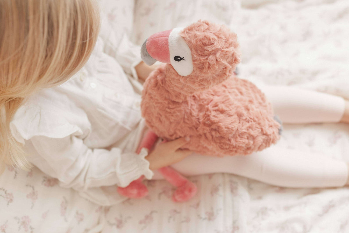 Child cuddling Francesca The Flamingo Weighted Teddy plush toy on a bed.