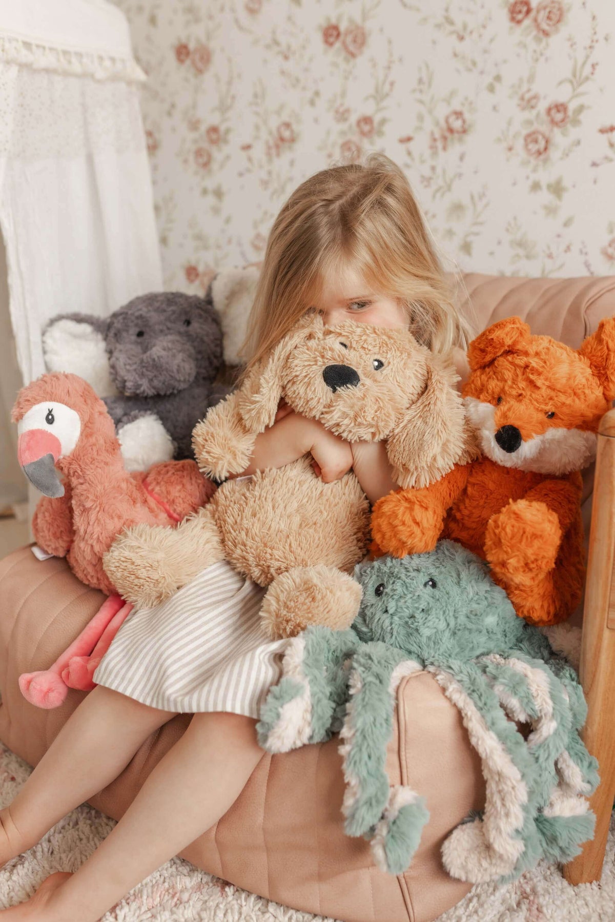 A girl hugs her Frankl The Weighted Fox teddy surrounded by other plush toys, promoting comfort and emotional wellbeing.