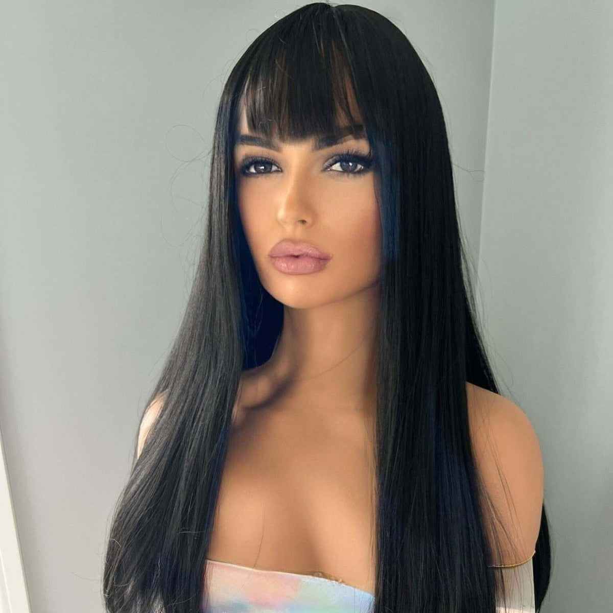 Mannequin head with long black wig and bangs on a plain background