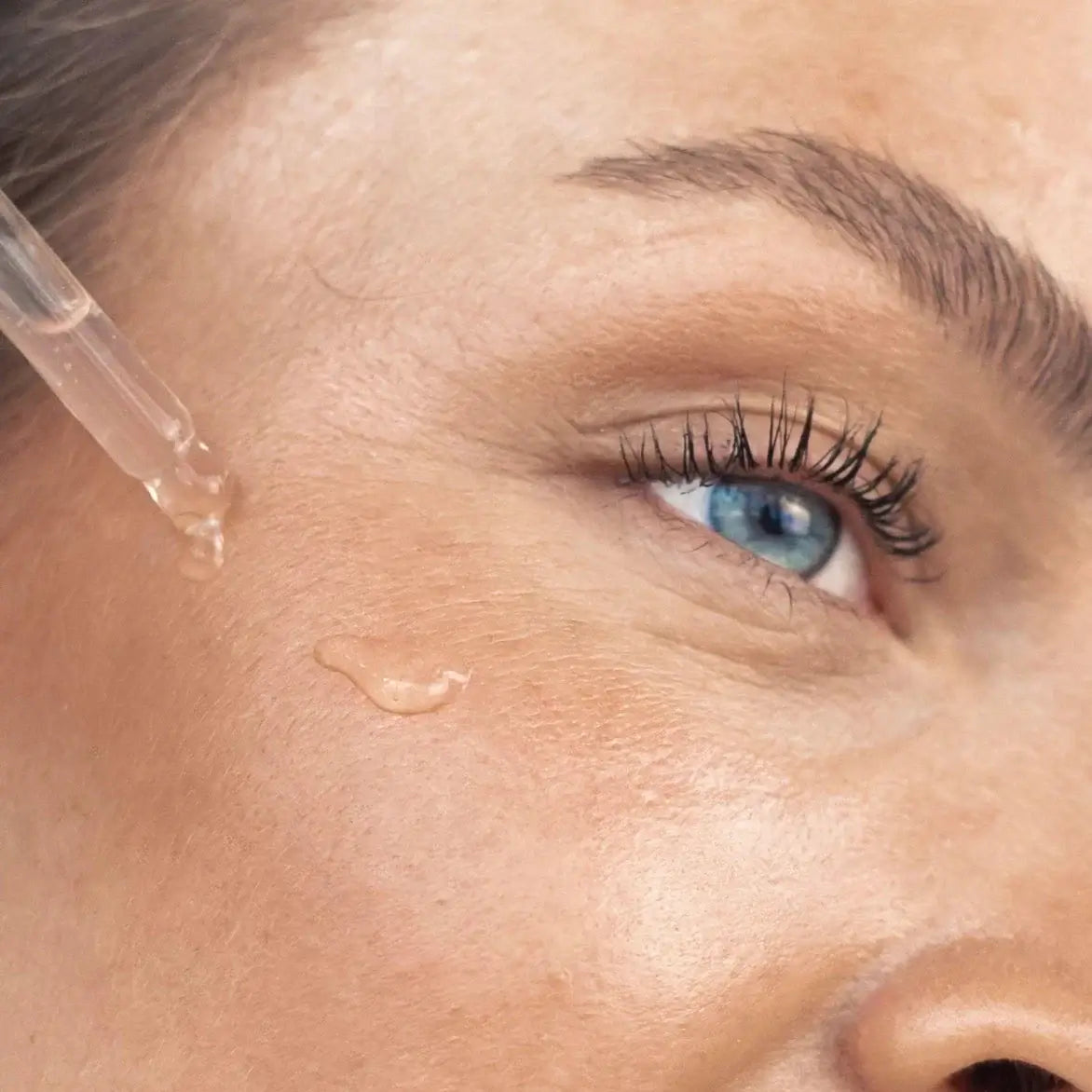 A close-up of a woman applying Glow Serum to her skin, emphasizing its luminous and hydrating effects.