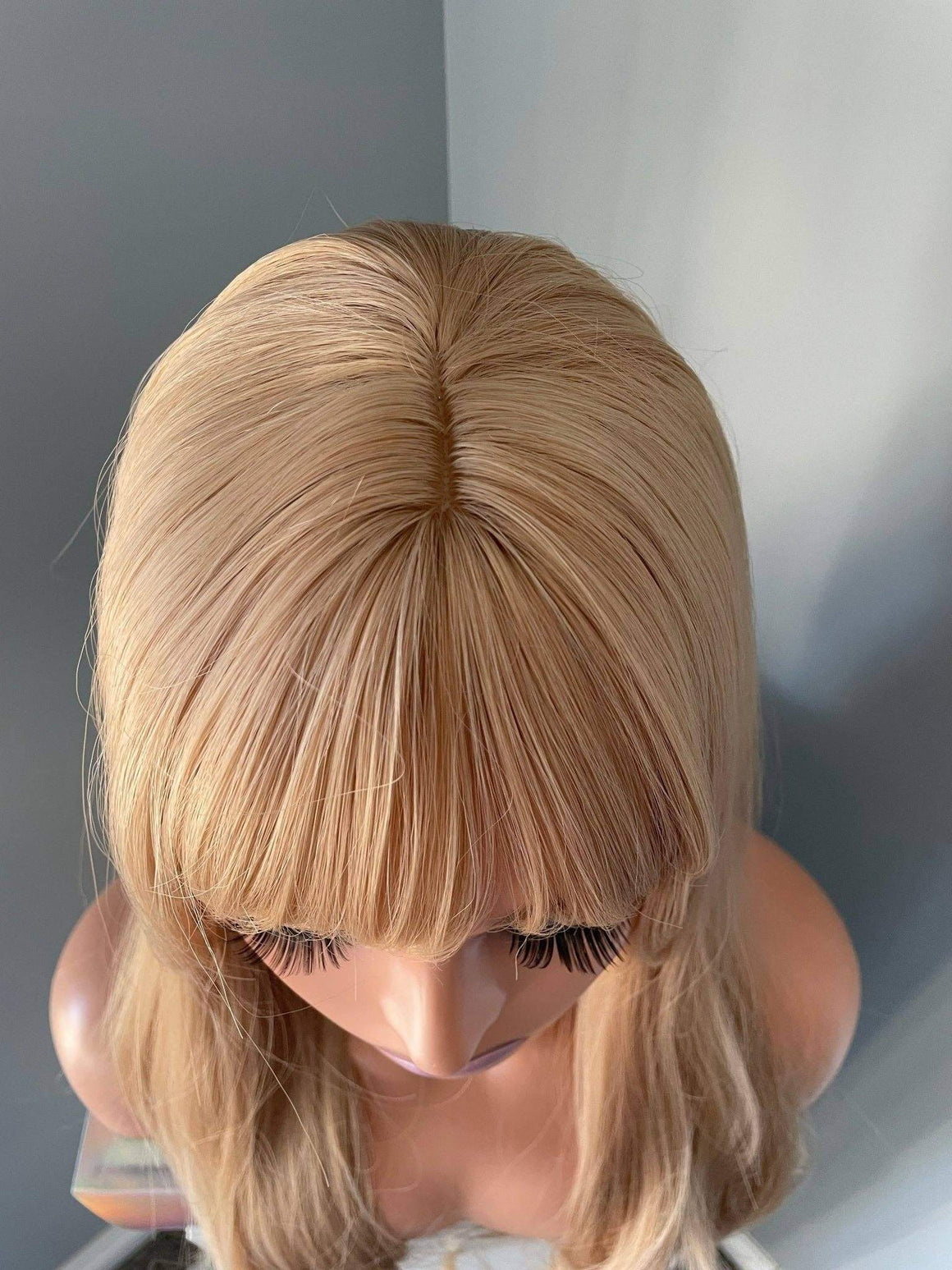 Blonde wig on a mannequin head against a neutral background