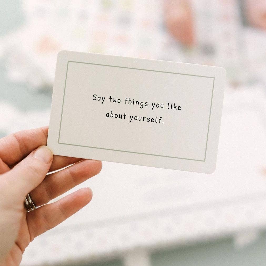 Hand holding a card with text 'Say two things you like about yourself.'
