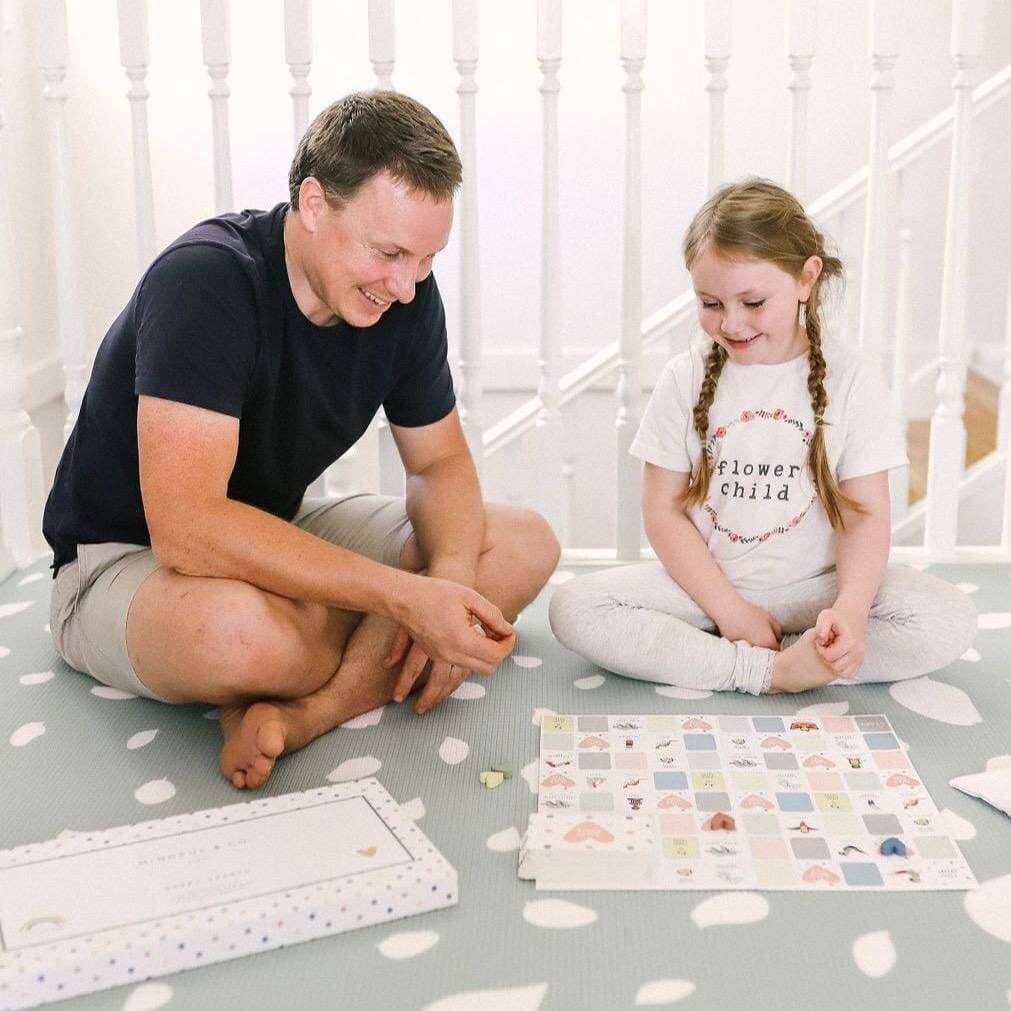 Man and young girl sitting on a polka dot rug playing with a board game.