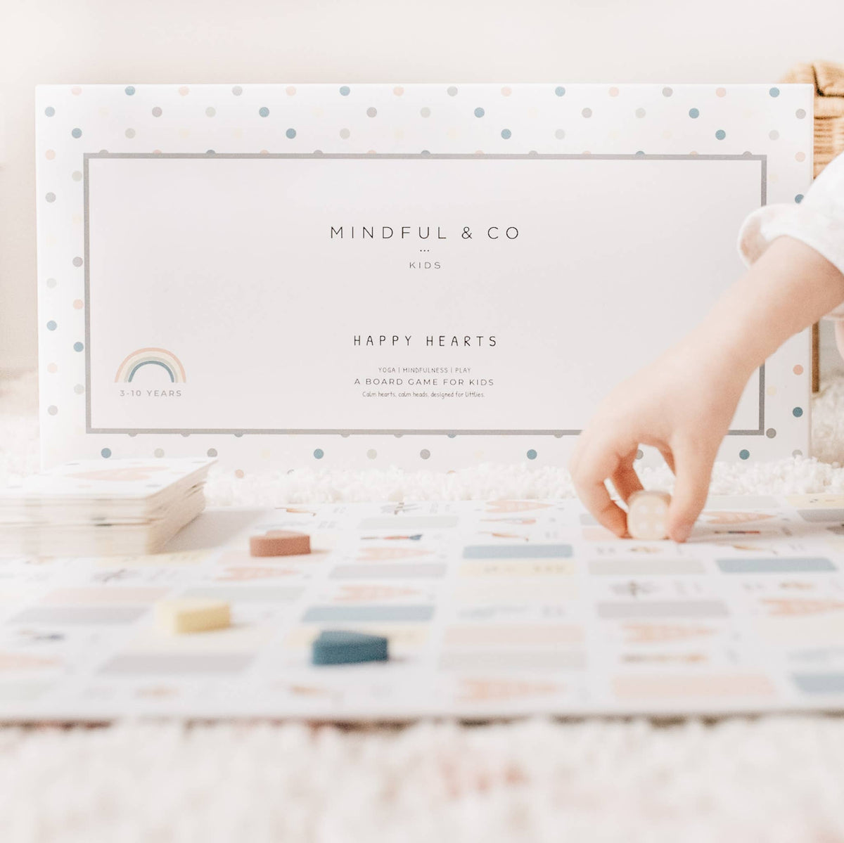 Mindful & Co kids card game packaging with a hand reaching for a card on a wooden surface.