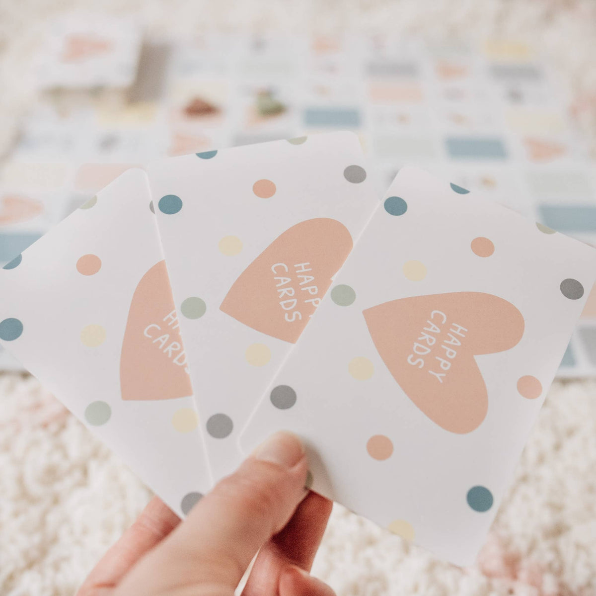 Three small cards with heart designs and 'Happy Cards' text held by a hand on a soft, blurred background.