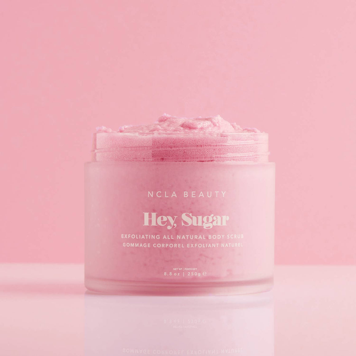 Pink jar of NCLA Beauty 'Hey, Sugar' exfoliating body cream on a pink background