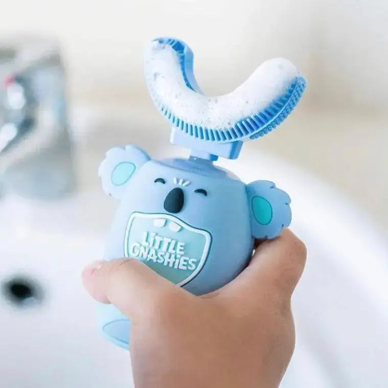 Blue children's toothbrush with a cartoon design held by a hand, on a blurred bathroom background.
