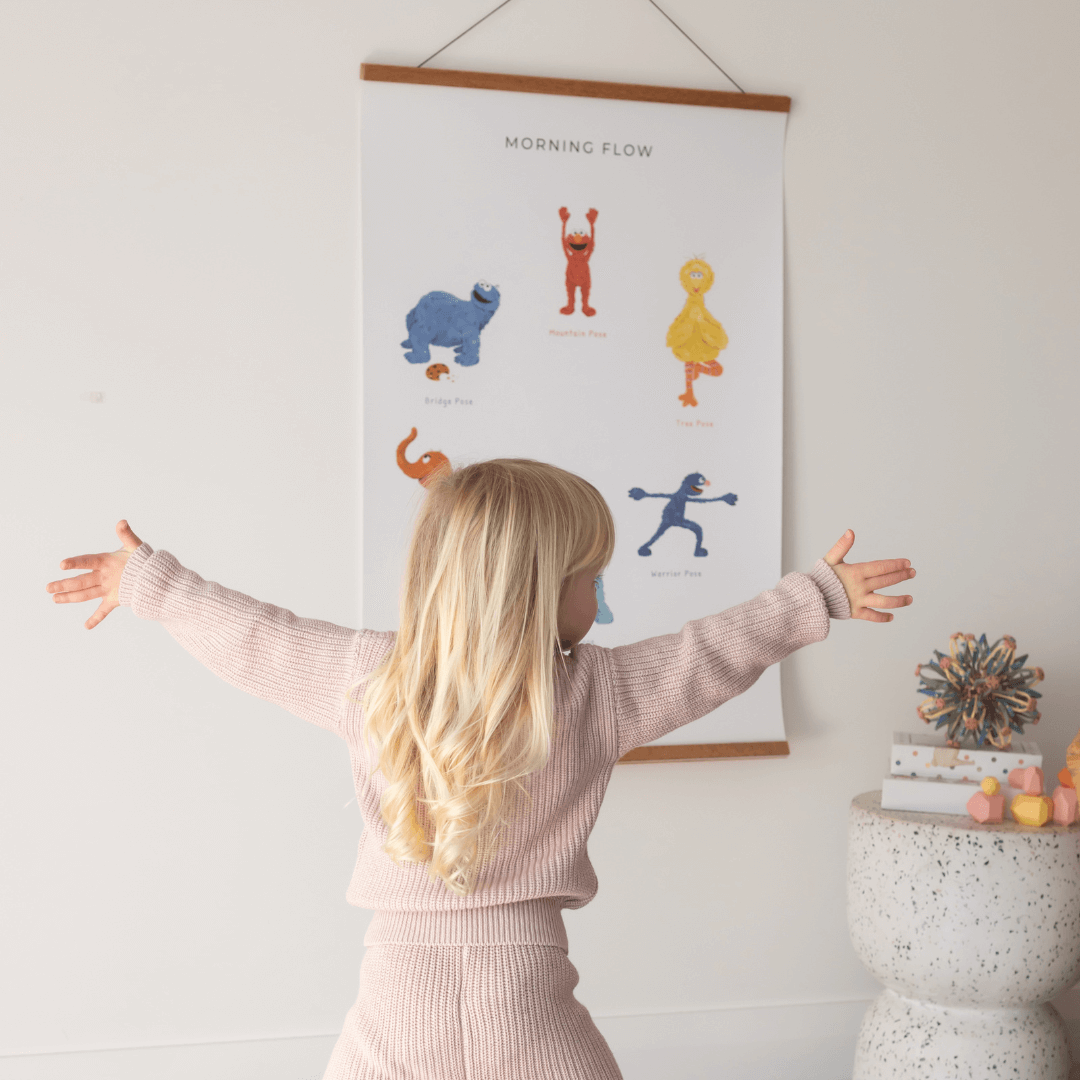 Child practicing yoga poses from the Double-sided Sesame Street Yoga Poses Print in a bright room.