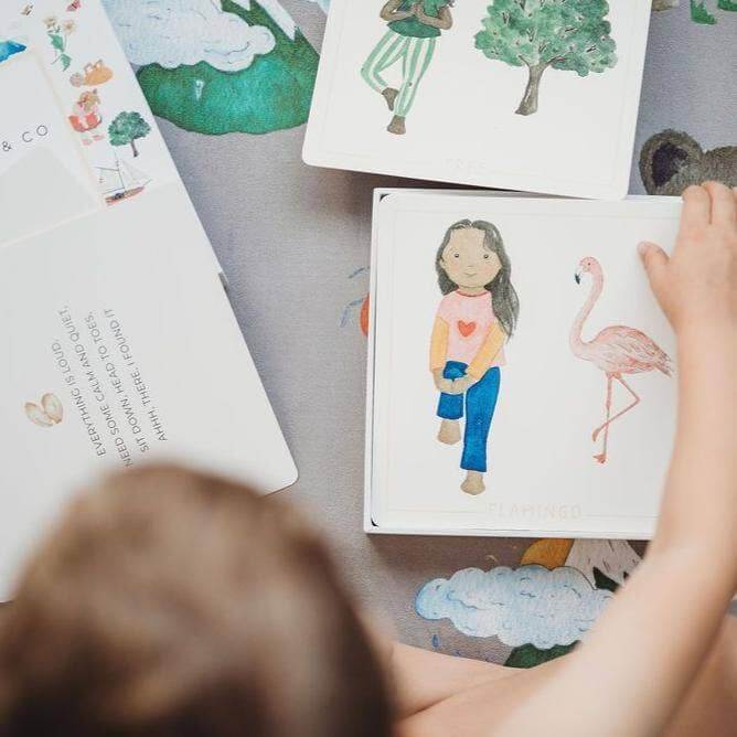 Child engaging with beautifully illustrated Yoga Flash Cards showing a girl and a flamingo.
