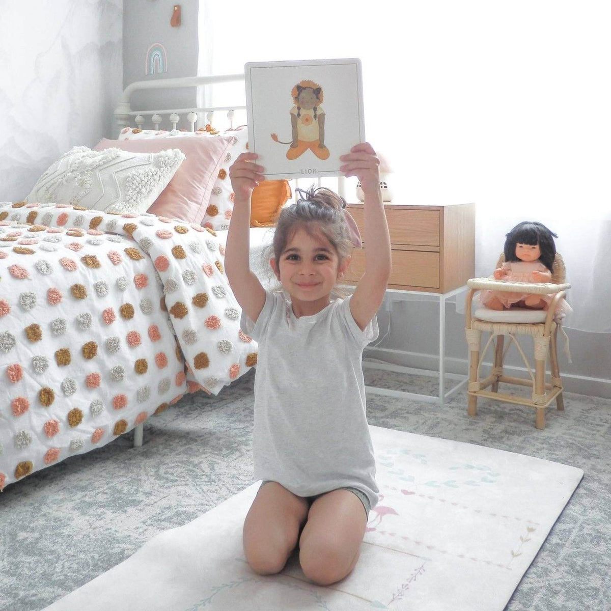 Child practicing yoga while holding Yoga Flash Cards in a cozy bedroom setting.