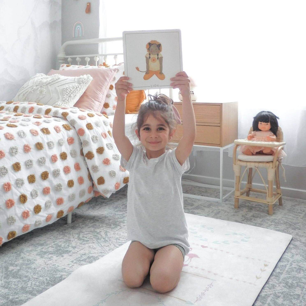 Child practicing yoga while holding Yoga Flash Cards in a cozy bedroom setting.