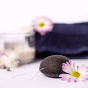 Black pumice stone with a string on a white surface with flowers and a blurred background