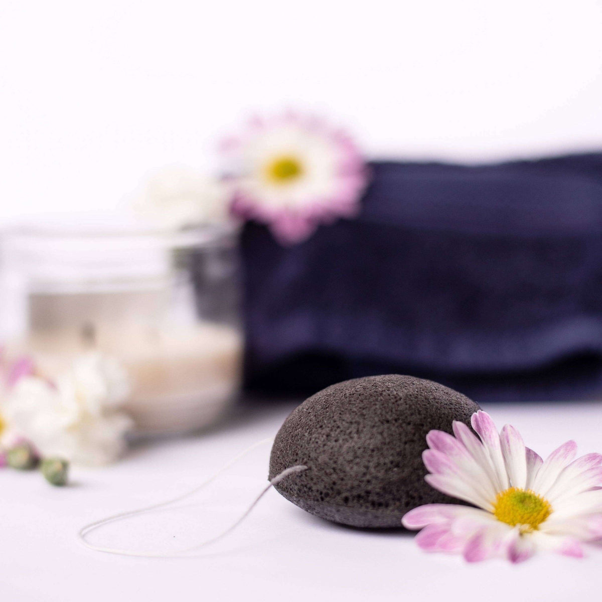 Black pumice stone with a string on a white surface with flowers and a blurred background