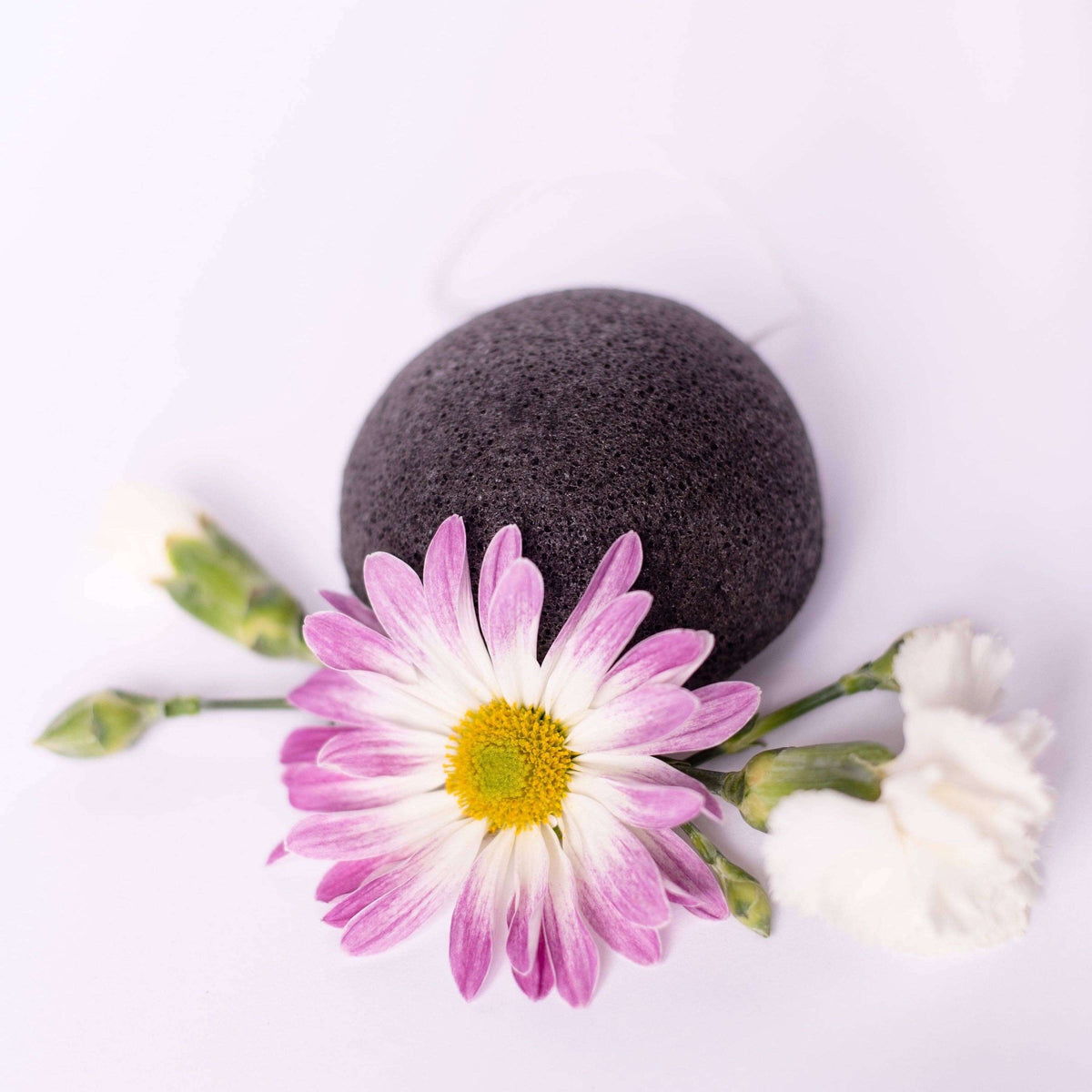 Black konjac sponge with a pink flower on a white background
