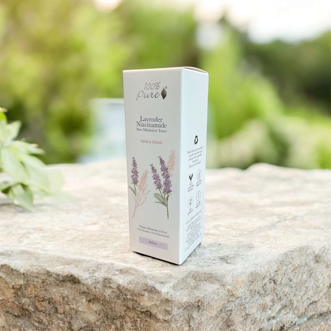 Lavender Niacinamide Pore Minimizer Tonique product packaging on a stone surface with greenery in the background.