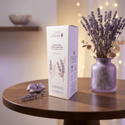 Lavender product packaging on a wooden table with a vase of lavender flowers.