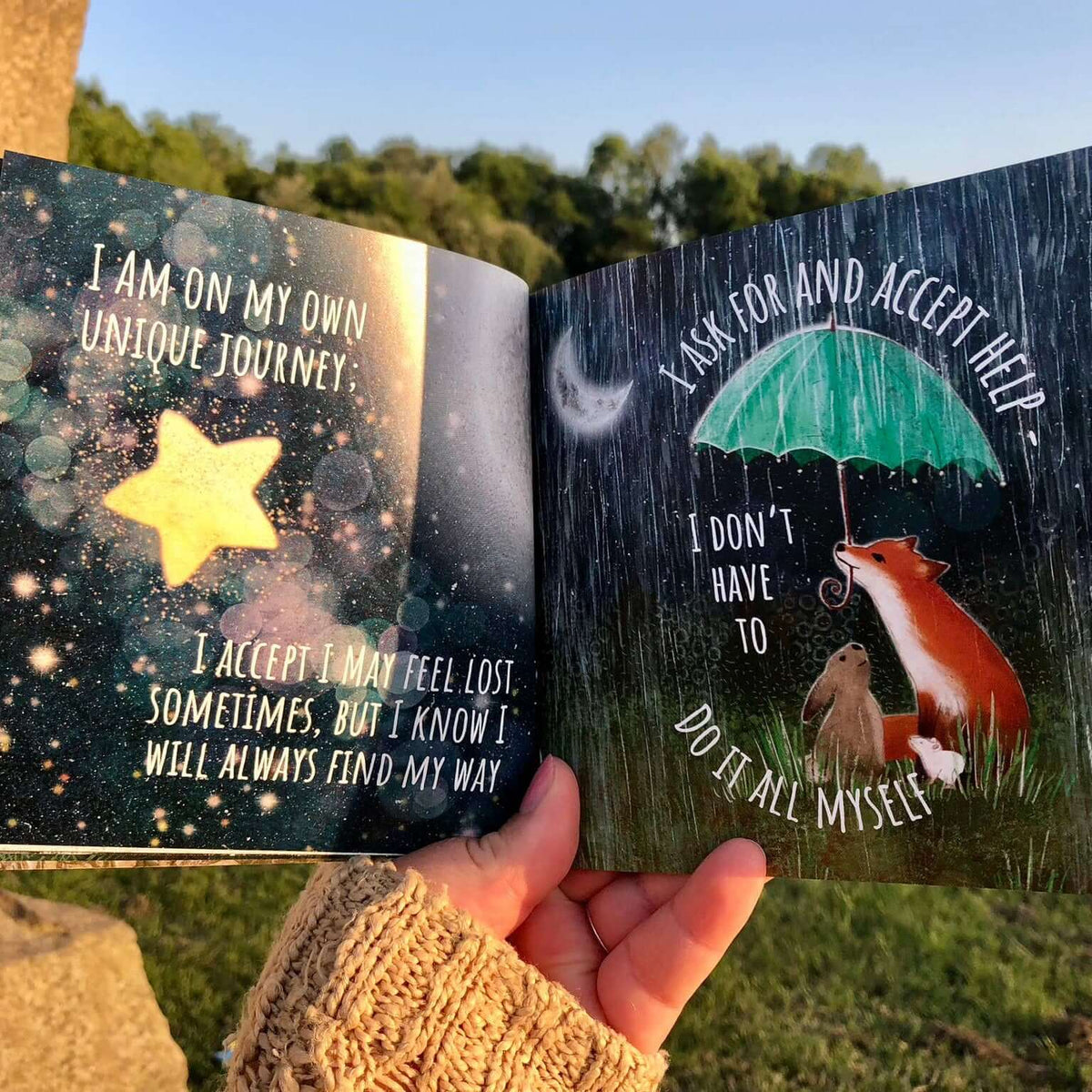 Open book with motivational quotes held by a hand outdoors.