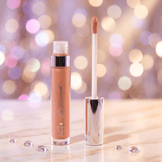 Lip gloss with applicator on a reflective surface against a bokeh light background