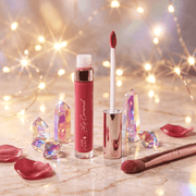 Lip gloss with applicator and rose gold brush on a marble surface with decorative lights in the background
