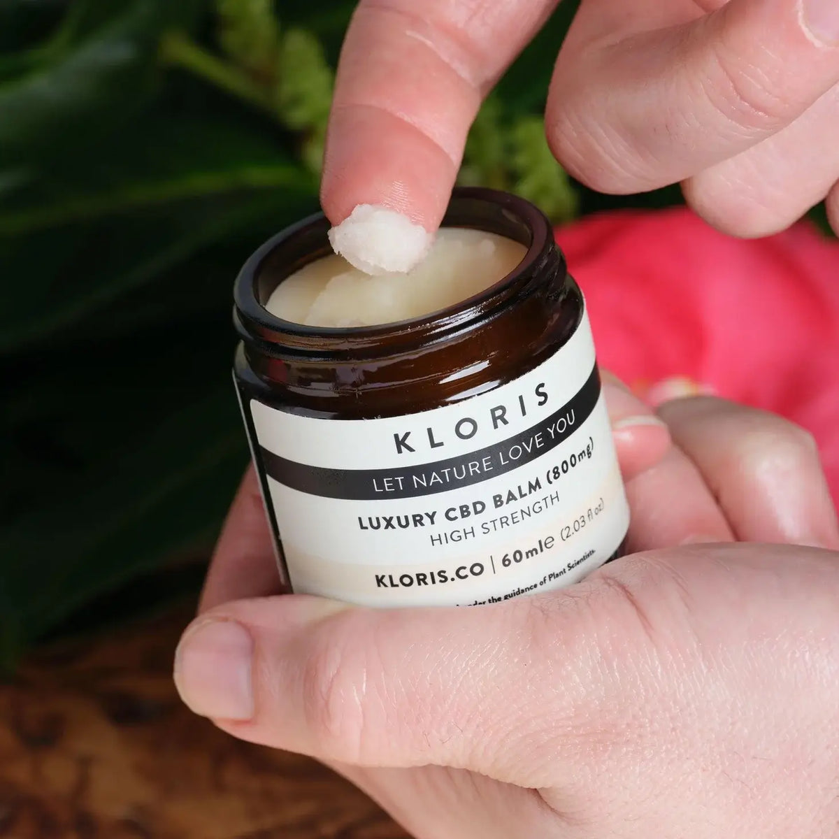 Hand holding a jar of Kloris CBD balm with a blurred background