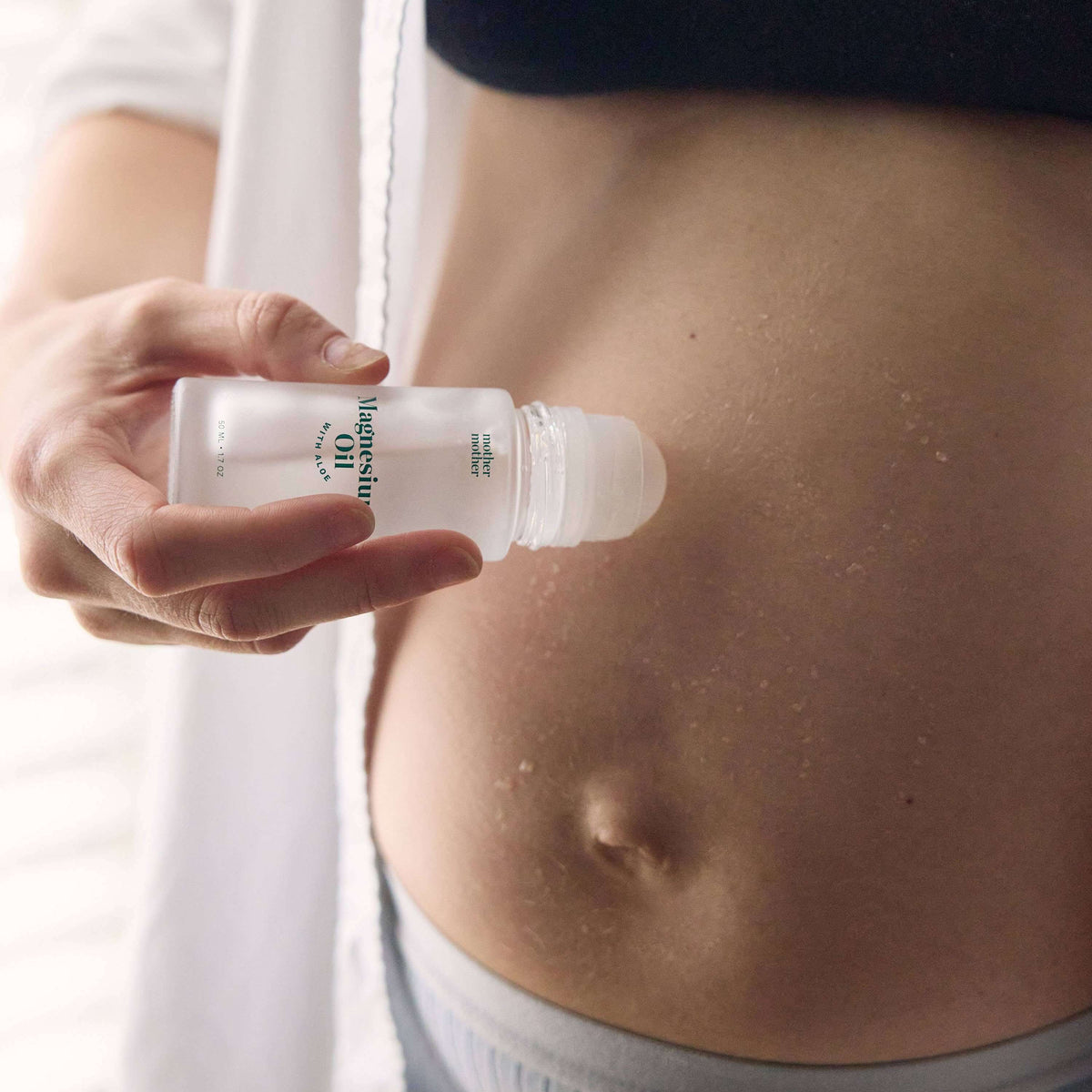 Person applying Magnesium Oil + Aloe Roller on their abdomen for targeted relief.