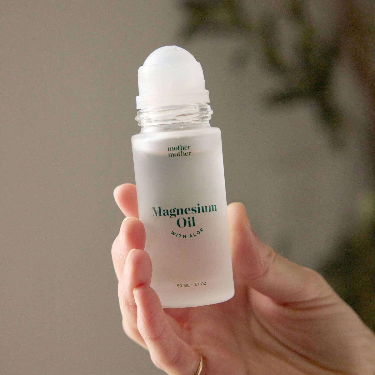 A hand holding a clear bottle of Magnesium Oil with Aloe Roller, featuring a roll-on applicator.
