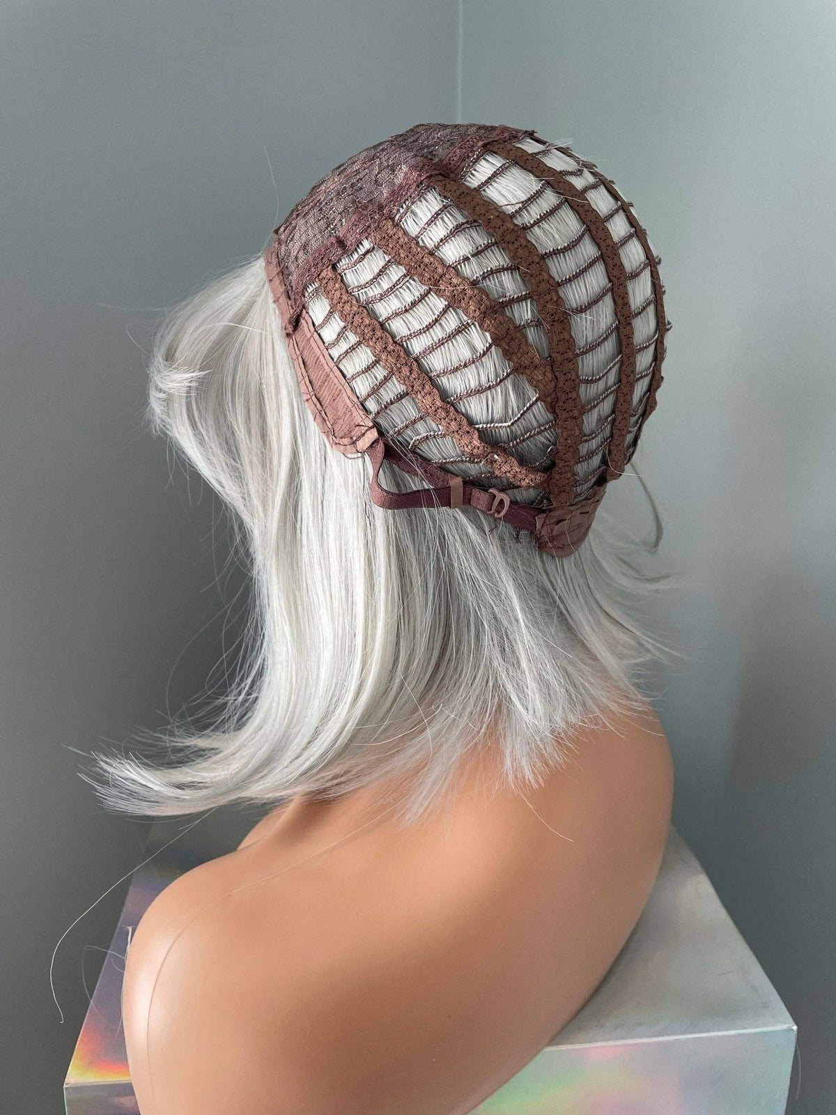 Mannequin head with a silver wig and brown mesh cap on a gray background