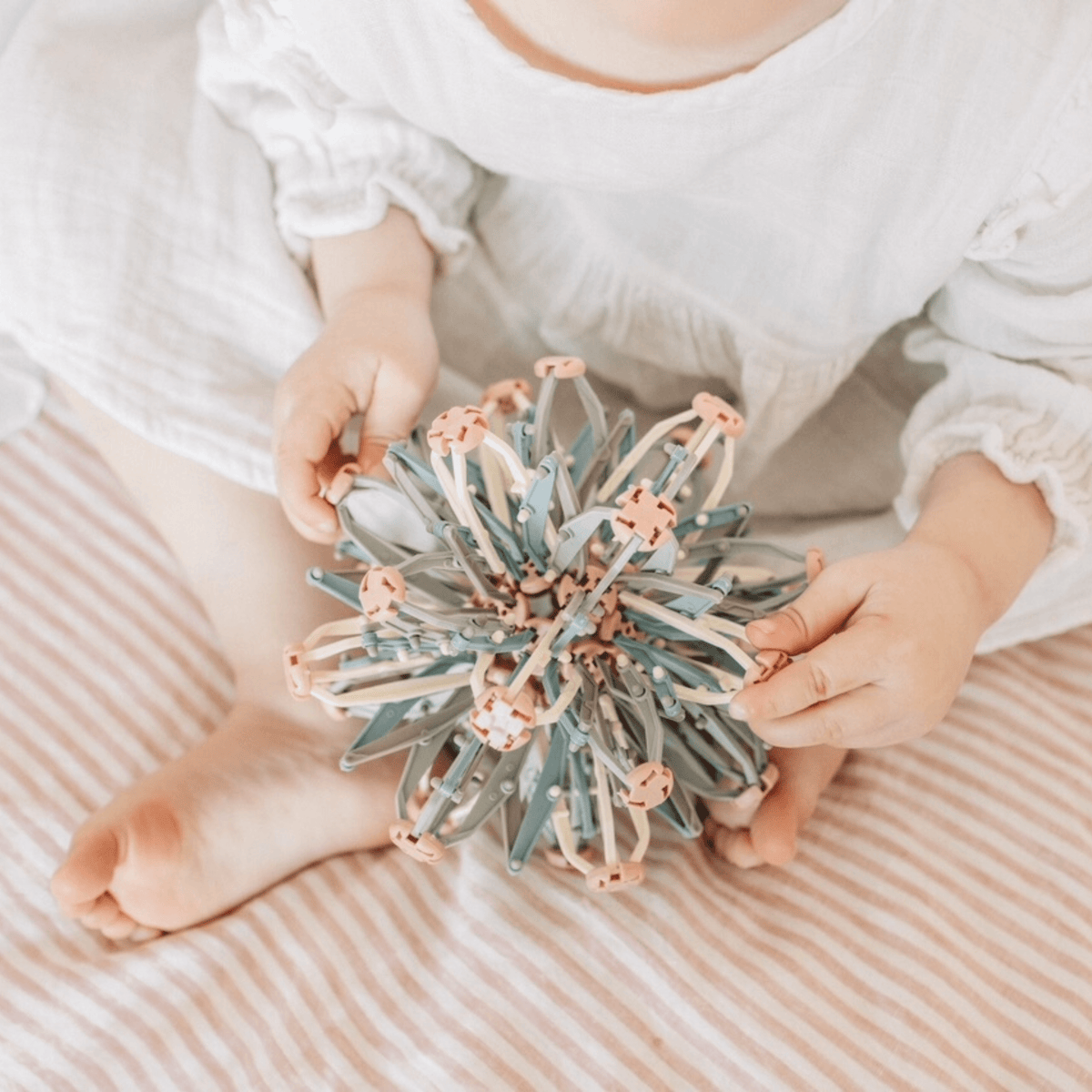 A child sitting on a striped blanket, holding a colorful Mindfulness Magic Ball, promoting mindful play and relaxation.