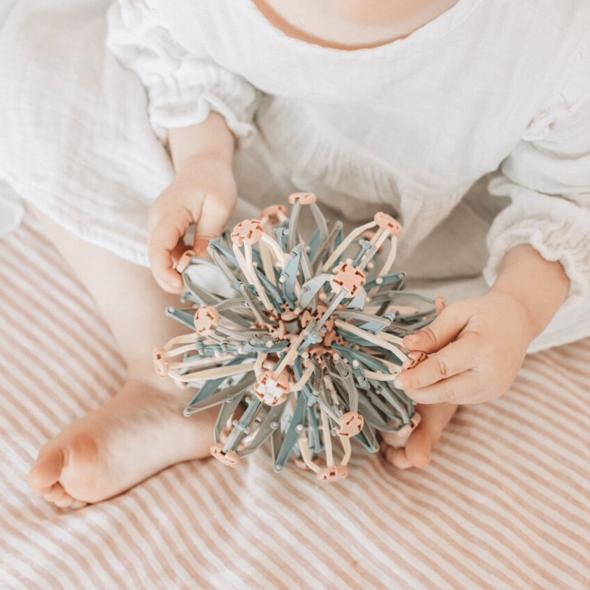 A child sitting on a striped blanket, holding a colorful Mindfulness Magic Ball, promoting mindful play and relaxation.