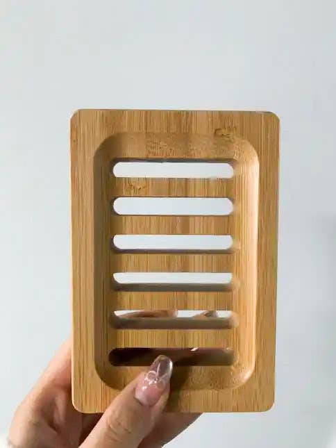 Wooden soap dish held by a hand against a light gray background