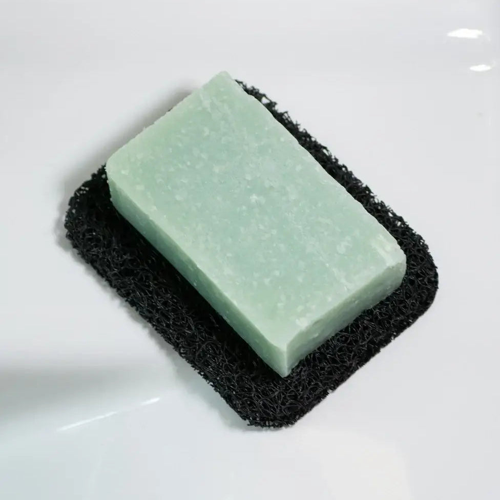 Green bar of soap on a black scrubber against a white background