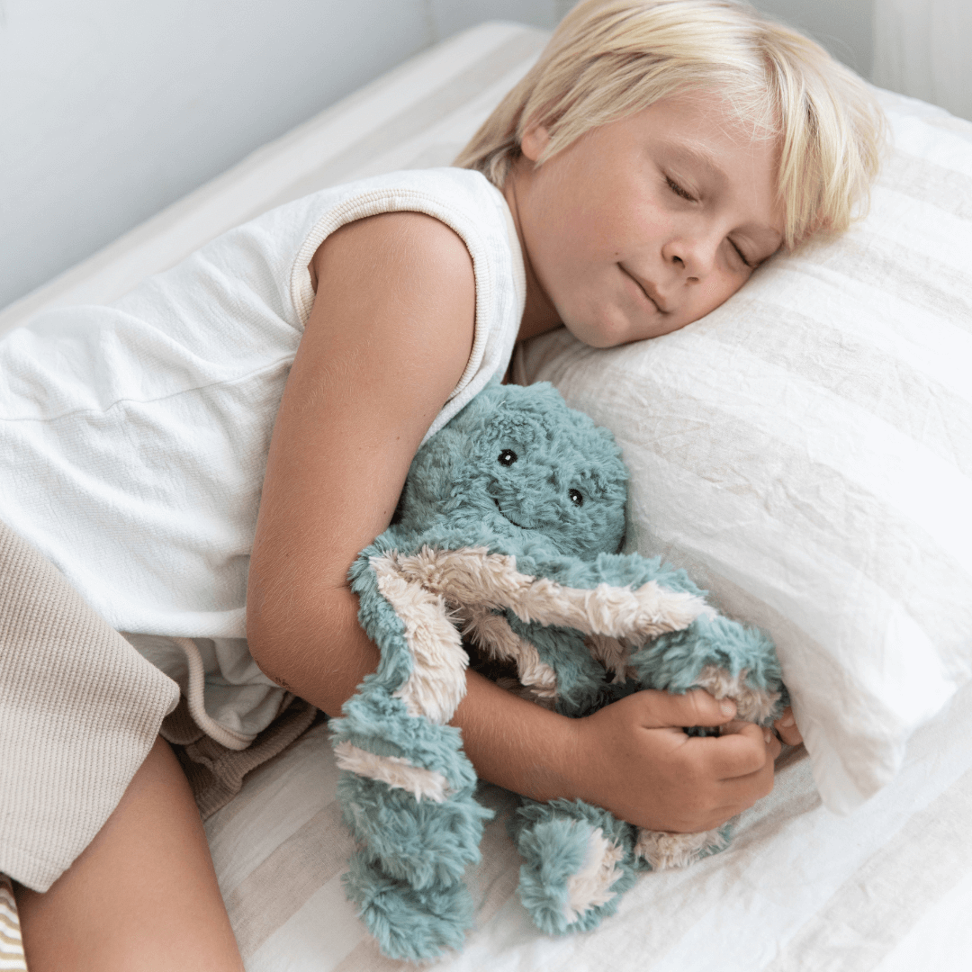 Child sleeping with a blue plush Weighted Teddy on a white pillow