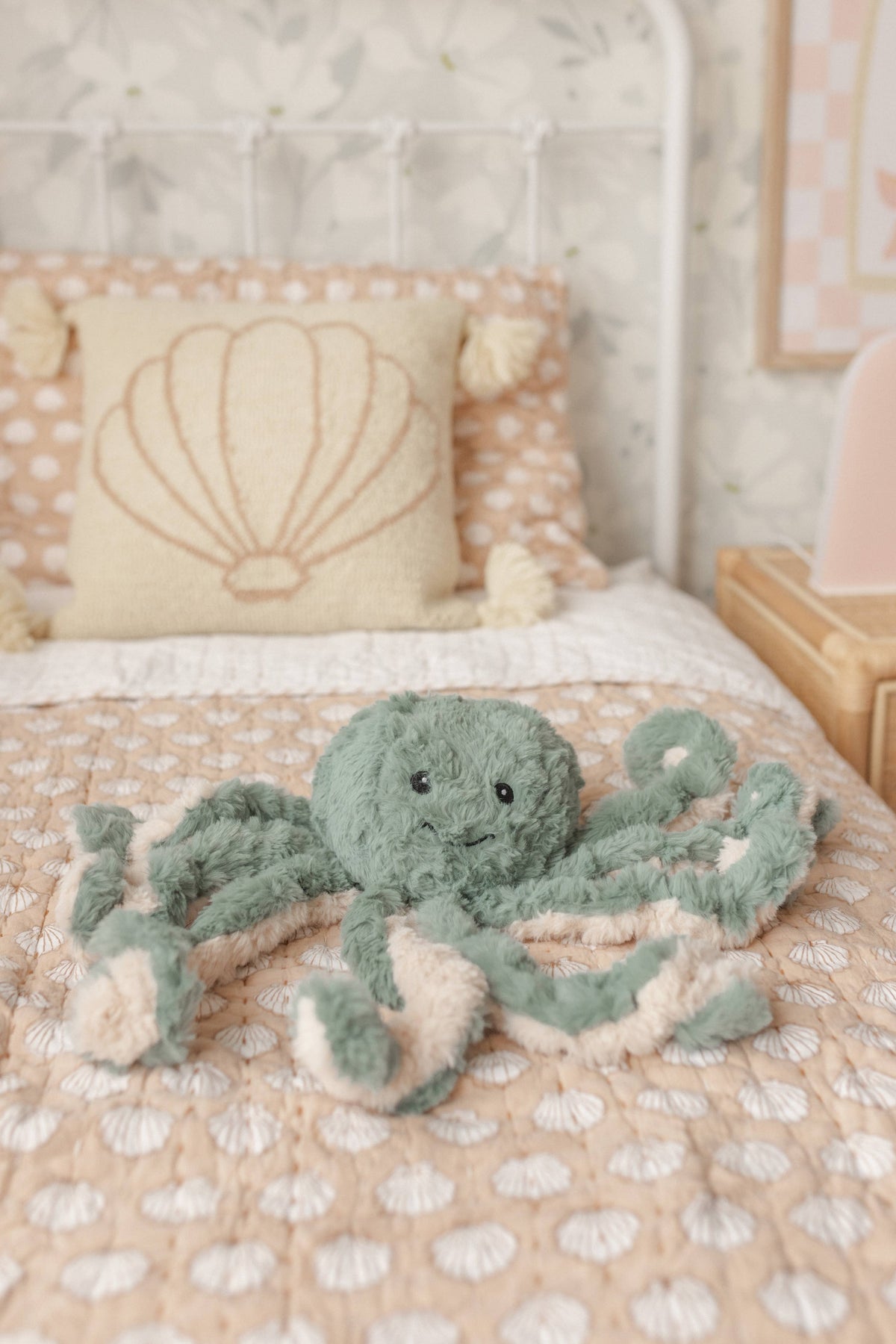Green plush octopus Weighted Teddy on a bed with shell-patterned pillows.