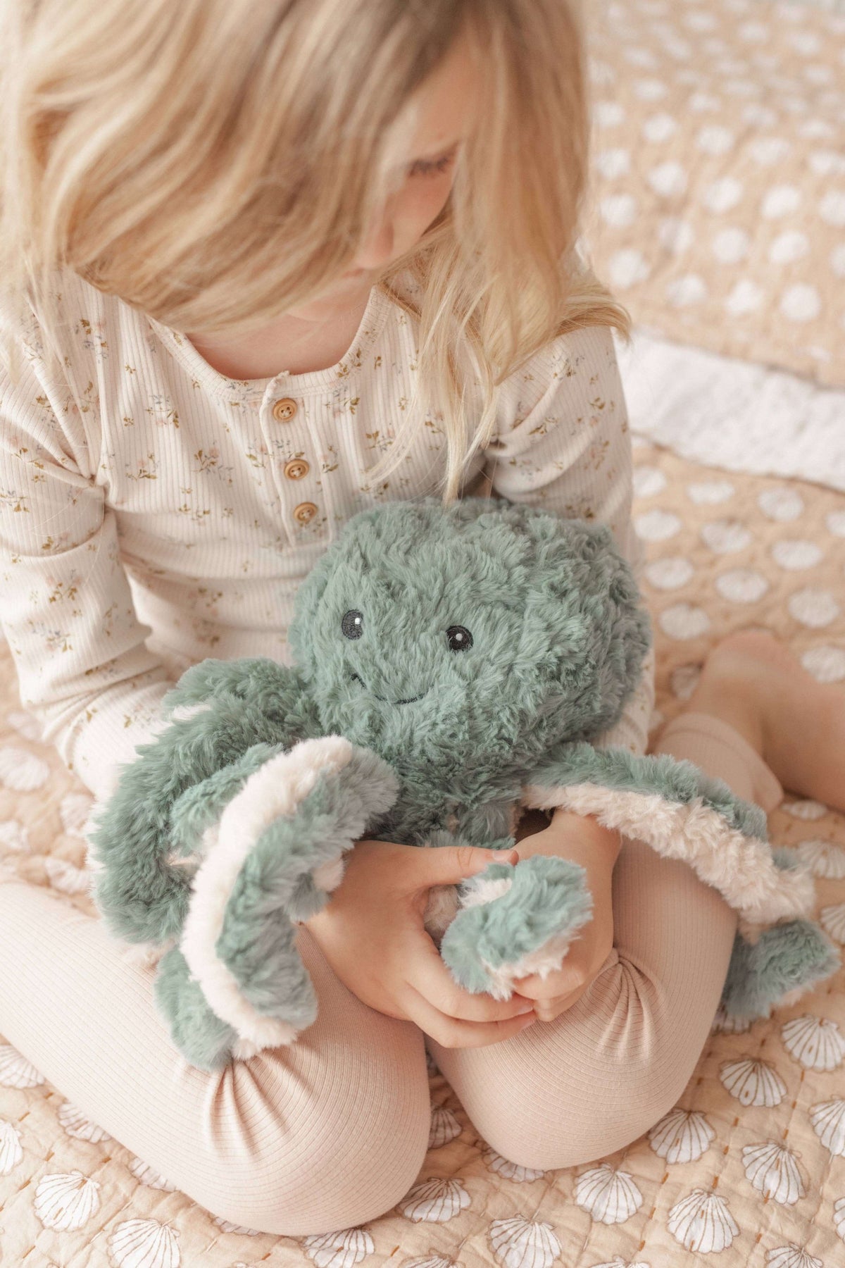Child holding a green plush Weighted Teddy on a soft surface
