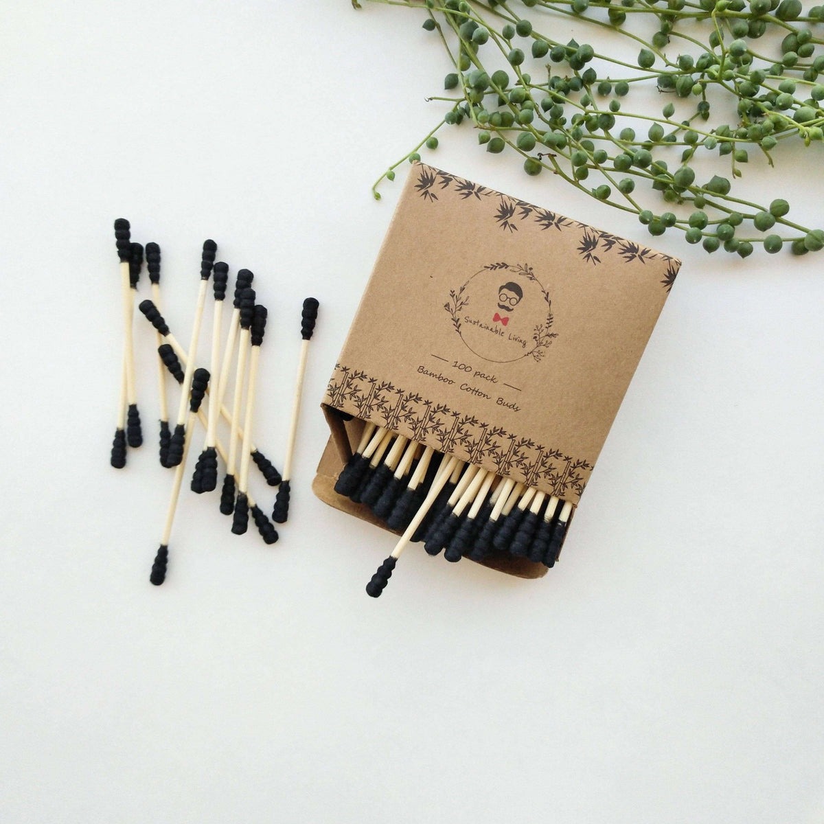 Matches with black tips and a brown matchbox on a white background with greenery.